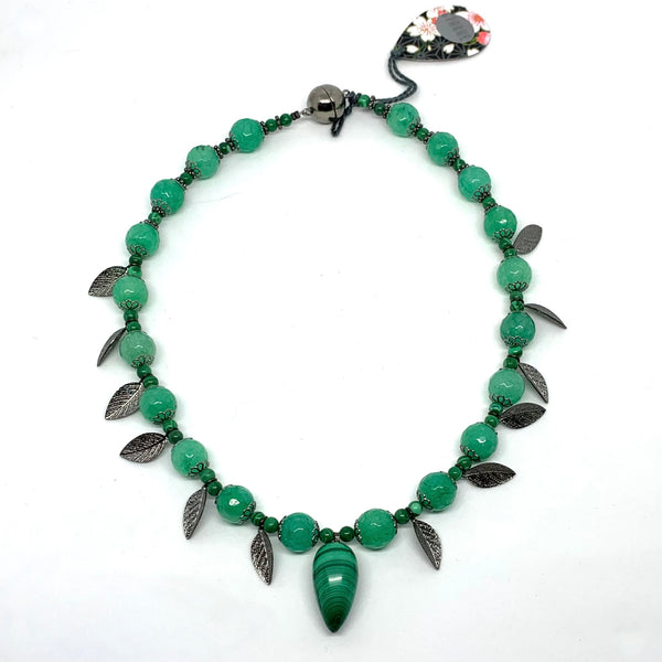 This one-of-a-kind necklace is handmade by Ottawa artisan Khalia Scott. It has natural, rare, polished and hardened semi-precious malachite beads and central pendant, faceted tinted agate beads, and small zinc alloy beads and findings.  It is strung securely by hand on a heavy coated multi strand tiger tail cord and has a spherical black metal two-part magnetic clasp. 16" long.