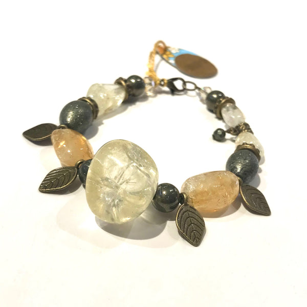 This one-of-a-kind bracelet is handmade by Ottawa artisan Khalia Scott. It is carefully crafted out of natural, polished semi-precious citrine stones, featuring a large chunky one at the centre. It also has spherical and oblong polished pyrite beads, faceted Czech crystals and oxidized bronze leaf charms. It is carefully strung by hand on a heavy coated multi-strand tiger tail cord and finished off with an oxidized bronze lobster clasp and findings. Size medium, approximately 8" in length.