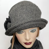 Find this One-of-a-kind, handmade “Cloche” hat by Ottawa artisan Sue Scott at Eclection Ottawa. The cloche embodies the beautiful 1920’s classic style and is fashioned here in a beautiful grey and black striped wool and cashmere blend fabric.  It is finished off with a handmade voluminous flower trim in the same fabric mixed with black wool blend fabric. It also features a Kasha lining that stops wind for added warmth and a small, top-stitched style-able brim. Size-medium: Approximately 22 ½’’  