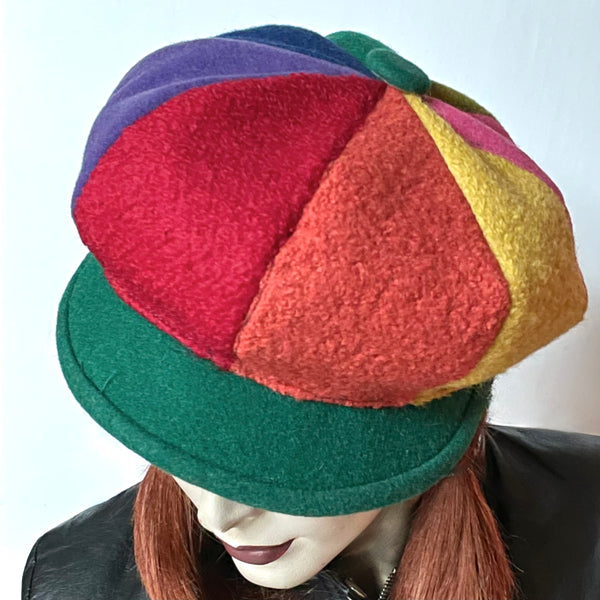  This Casquette is fashioned in a mix of different fabrics that goes from wool flannel,  cashmere and wool blend to 100% wool coating. The shape is an eight-part crown, with some volume and a front peak where each part of the crown is made with a different colour. Red, candy pink, purple, indigo blue, forest green, chartreuse, yellow and Orange. Forest green peak and covered button on top. Wind-resistant lining. Size L: 23 1/4’’ with an elastic in the back. 