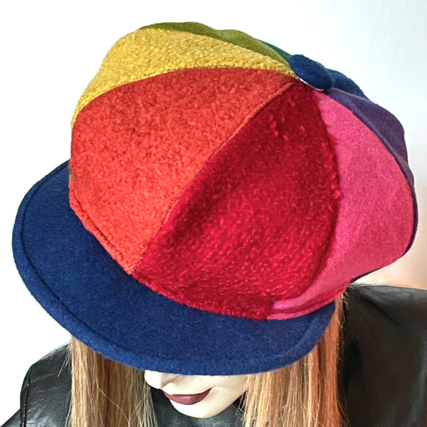  This Casquette is fashioned in a mix of different fabrics that goes from wool flannel,  cashmere and wool blend to 100% wool coating. The shape is an eight-part crown, with some volume and a front peak where each part of the crown is made with a different colour. Red, candy pink, purple, indigo blue, forest green, chartreuse, yellow and Orange. Indigo blue peak and covered button on top. Wind-resistant lining. Size L: 23 1/2’’ with an elastic in the back.