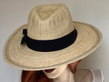 Find this charming Fedora hat at Eclection Ottawa. The “Jonni” is made out of braided paper with a naturally variegated looking shades of natural and light tan, and trimmed with a large black grosgrain ribbon. The shape is a classic fedora crown, and a large flat wired brim with top stitches toward the edge. With an adjustable elastic inside. Size of 22 1/4" to smaller. Brim 3 1/2. Crown 4 3/8".