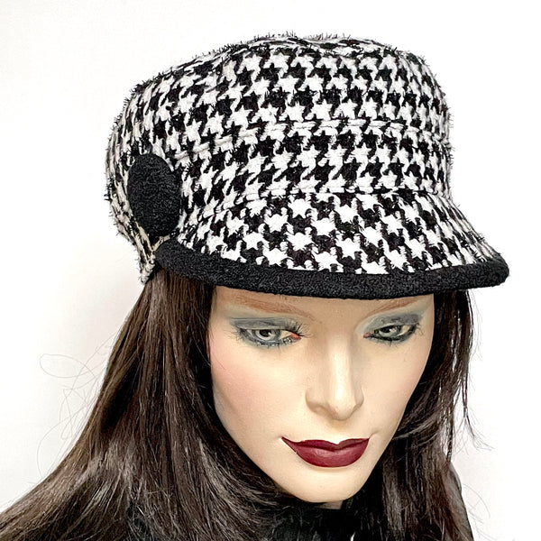 This one-of-a-kind hat, handmade by local artisan Sue Scott, is called the "Crumper". It is fashioned in a woven houndstooth wool blend in black and white colours. The shape is a straight-sided, flat-topped crown, with a classic front peak. It is embellished with a large button trimming covered in coordinated black boiled-wool fabric that is repeated on the underside of the peak. Fully lined with windproof Kasha lining. Size-medium approx. 22 1/4" with an elastic at the back for easy fit.