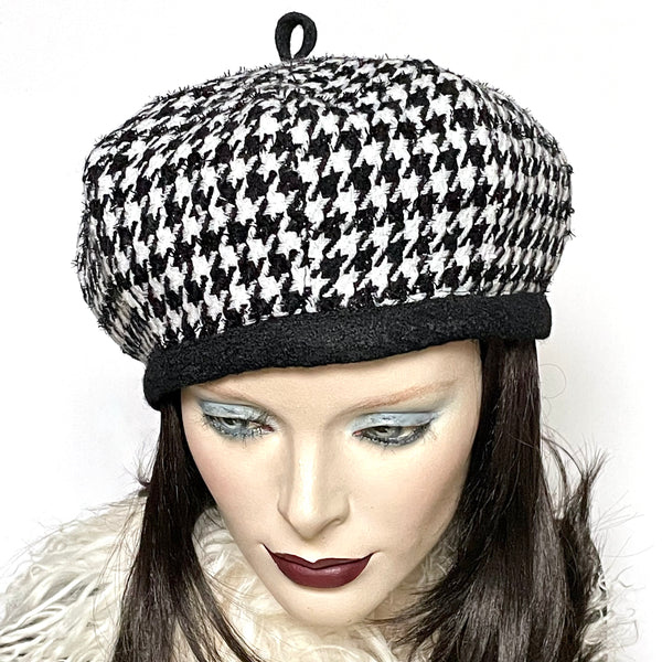 This one-of-a-kind hat, handmade by local artisan Sue Scott, is called the "Gigi". It is fashioned in a woven houndstooth wool blend in black and white colours, with some lurex woven in. The shape is an eight-part voluminous crown that gives body to this beret and the trim is a fun loop on top made in coordinated black boiled-wool fabric, and repeated at the headband. Fully lined with a windproof Kasha lining. Size-medium: Approx 22 ½’’ with an elastic cord inside the headband to go smaller.