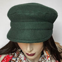 One-of-a-kind, handmade “Captain” hat by Ottawa artisan Sue Scott. It is fashioned in a rich and cozy forest green wool blend that's perfect to add a little colour in the colder months. The shape is a classic two-part crown with some volume and a smart front peak that protects you from snowflakes. It is fully lined with a satiny, flannel-backed Kasha lining that’s easy on the hair and stops wind for added warmth. Size-medium: Approximately 22 1/2".    Dry Clean Only