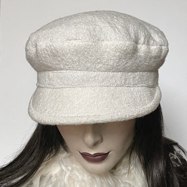 One-of-a-kind, handmade “Captain” hat by Ottawa artisan Sue Scott.  It is fashioned in a classic winter white wool blend with a beautifully soft and cozy texture in an easy-to-wear off-white colour that you will reach for all winter. The shape is a classic two-part crown with some volume and a nice smart peak in the front that protects you from snowflakes. It is fully lined with a thick, tightly woven wind-stopping kasha lining for added warmth. Size-medium: Approximately 22 ½.’’   