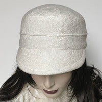 This one-of-a-kind hat, handmade by local artisan Sue Scott, is called the "Crumper". It is fashioned in a classic winter white wool blend with a beautifully soft and cozy texture in an easy-to-wear off-white colour. The shape is a straight-sided, flat-topped crown, with a classic front peak that conveniently keeps snow off your eyelashes. It is fully lined with a thick wind-stopping kasha lining for added warmth. Size-medium: Approximately 22 1/2" Dry clean only.