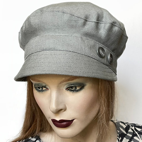 One-of-a-kind, handmade “Captain” hat by Ottawa artisan Sue Scott. It is fashioned in 100% medium-weight linen in a sophisticated and easy-to-wear medium grey shade perfect as the finishing touch to your summer outfit. Its shape is a classic two-part crown with some volume and a nice smart peak in front that protects from the sun. It is finished off with matching vintage buttons on the sides and is fully lined with satin. Size medium at approximately 22 1/2".  