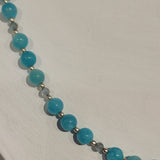 Closeup of strand of bright turquoise amazonite beads spaced with small pale blue crystals and tiny silver beads