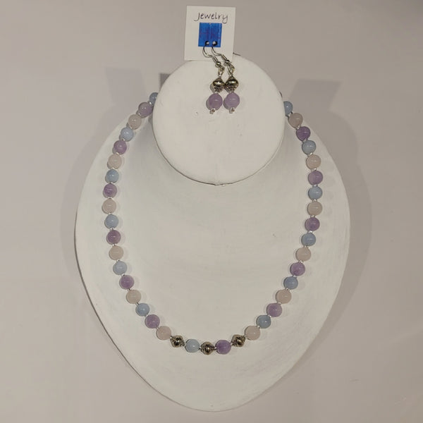 Single strand necklace of pastel pink, blue, and purple natural stones spaced with clear seed beads and featuring 3 silver beads at the bottom, and matching short drop earrings of pastel purple amethyst and silver beads