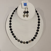 Single strand necklace of shiny black hyperstein beads in flat round shape spaced with small round silver beads and featuring three larger silver beads with swirl pattern on the bottom, and a matching set of short drop earrings 