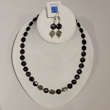 Single strand necklace of shiny black hyperstein beads in flat round shape spaced with small round silver beads and featuring three larger silver beads with swirl pattern on the bottom, and a matching set of short drop earrings 