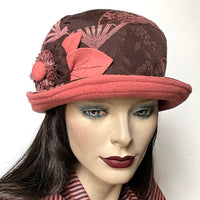 One-of-a-kind, handmade “Cloche” hat by Ottawa artisan Sue Scott. It is fashioned in a cozy wool blend tapestry fabric with a cocoa background and cameo pink fan design and matching pink fabric at the under brim. It is finished off by a hand-sewn flower rosette trim in the same fabrics. It is lined with a satiny, flannel-backed and windproof Kasha lining that’s easy on the hair and features a flexible top-stitched brim that can be styled as you like. Size small/medium: Appr 21 3/4’’   Dry Clean 