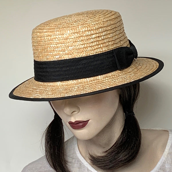 Find this flattering boater hat at Eclection Ottawa. The “Augie” is made out of 100% braided natural straw and trimmed with a black grosgrain ribbon and a flat bow at the back. The shape is an oval flat top crown and a flat, straight brim with grosgrain edge. Wide elastic interior band. Size Medium 22 1/2", Brim 2 1/4", Crown 3 7/8"
