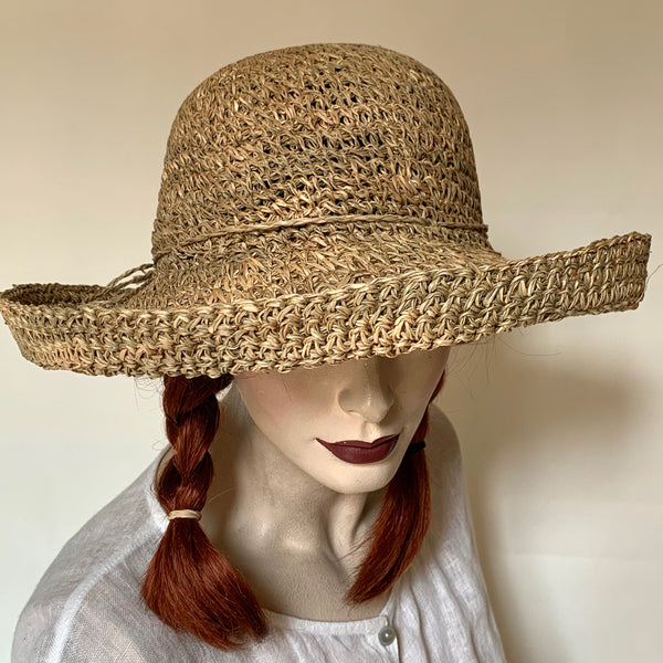 Find this flattering and charming hat at Eclection Ottawa. The “Lolakoï” is crafted out of 100% crocheted naturally variegated seagrass in shades of olive and taupy colour, and finished off with twisted seagrass trim knotted in a bow. The shape is a flexible round cloche crown, and a downward kettle brim with a 1" edge that flips up. Size of 22 1/2" to smaller. Brim 3 1/4". Crown 4 1/2".