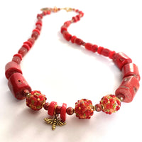 This one-of-a-kind necklace is handmade by Ottawa artisan Khalia Scott. It is carefully crafted out of tinted coral, large and beautifully textured lampwork beads, small glitter glass beads in a rich tone of red, tinted agate and finished off with a gold plated bee charm, faceted separator beads and findings. It is strung securely by hand on a heavy coated multi-strand tiger tail cord and has a gold-plated clasp. It is measuring 25 3/4". Second picture