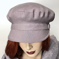 Find this handmade “Captain” hat by Ottawa artisan Sue Scott, at Eclection Ottawa. It is fashioned in 100% lighter-weight linen in an easy-to-wear dusty lilac shade that brings colour to your spring and summer outfit. Its shape is a classic two-part crown with some volume and a nice smart peak in front that protects from the sun. It is finished off with matching vintage buttons on the sides and is fully lined with satin. Size medium at approximately 22 1/2".  
