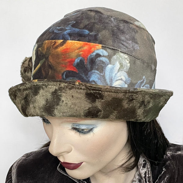 Find this One-of-a-kind, handmade “Cloche” hat by Ottawa artisan Sue Scott at Eclection Ottawa. It is fashioned in a beautiful Baroque floral print in polyester panne velvet in tones of rust, greys, sage, and plum. Its under-brim is a polyester faux fur in a dark sage shade with a handmade flower trim in the same fabric. It is lined with a satiny Kasha lining that stops wind for added warmth and features a small, style-able brim. Size-medium: Approximately 22 ½.’’  Dry clean only. 