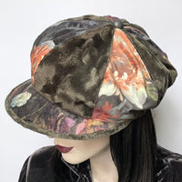 Find this one-of-a-kind Casquette, handmade by local artisan Sue Scott at Eclection Ottawa. It is fashioned in a beautiful Baroque floral print in polyester panne velvet in tones of rust, greys, sage and plum mixed with a polyester faux fur in a dark sage shade with a swirl texture that also graces the under-peak. The shape is an eight-part crown, with some volume and a front peak. Antique metal button trim. Windproof lining. Size medium-large: Approximately 22 1/2’’ with an elastic in the back.