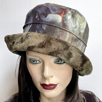 Find this one-of-a-kind, handmade “Jojo” hat with a Stella brim by Ottawa artisan Sue Scott at Eclection Ottawa. It is fashioned in a beautiful Baroque floral print in polyester panne velvet in tones of rust, orange, blue-greys, sage, taupe and plum. Its under-brim is a polyester faux fur in a dark sage shade with a swirl texture. The Stella brim is flexible brim and can be styled easily. It is fully lined with a thick and tightly woven wind proof Kasha lining. Size-medium: 22 ½.’’