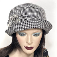 Find this handmade “Cloche” hat by local artisan Sue Scott at Eclection Ottawa. It is fashioned in mid-weight 100% linen in a timeless black and white houndstooth pattern that will never go out of fashion. The shape is a classic rounded cloche crown that features a flexible brim that can be styled to your tastes.  This hat is finished off with a matching hand-sewn rose trim with a covered button at its center and is fully lined with satin.  Size-medium: approximately 22 ½.’’ 
