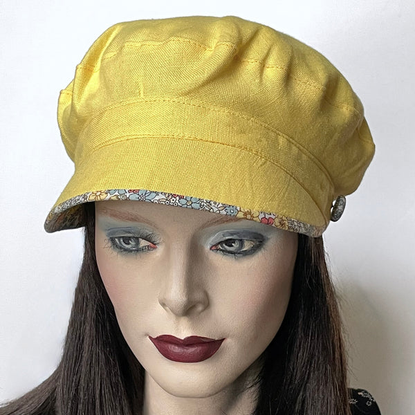 Find this handmade “Captain” hat by Ottawa artisan Sue Scott, at Eclection Ottawa. It is fashioned in mid-weight 100% linen in a beautiful lemon-yellow shade. Its shape is a classic two-part crown with some volume and a nice smart peak that features a floral under-peak in coordinated cotton fabric tones of chambray, yellow and soft corals on an off-white background. It is finished off with covered button trim that repeats the fabric of the under-peak. Fully lined. Size medium, approx 22 1/2".  