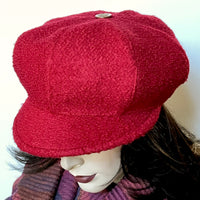Find this one-of-a-kind Casquette, handmade by local artisan Sue Scott at Eclection Ottawa. It is fashioned in a fun deep red wool blend fabric with a rich and cozy boucle texture which is perfect for adding a bit of colour in wintertime. The shape is an eight-part crown, with some volume and a front peak. It is finished off with a vintage metal button on top and is fully lined with a windproof Kasha lining. Size medium-large: Approx 22 1/2’’ with an elastic in the back. 