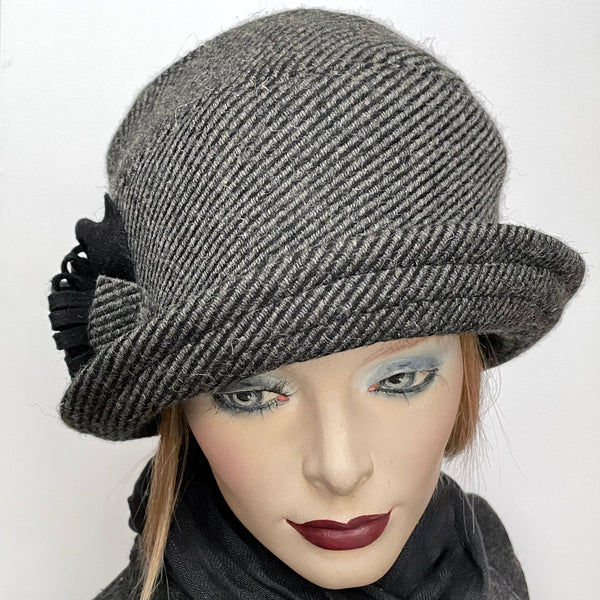 Find this One-of-a-kind, handmade “Cloche” hat by Ottawa artisan Sue Scott at Eclection Ottawa. The cloche embodies the beautiful 1920’s classic style and is fashioned here in a beautiful grey and black striped wool and cashmere blend fabric.  It is finished off with a handmade voluminous flower trim in the same fabric mixed with black wool blend fabric. It also features a Kasha lining that stops wind for added warmth and a small, top-stitched style-able brim. Size-medium: Approximately 22 ½’’  