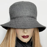 Find this handmade "Nina" bucket hat by local artisan Sue Scott at Eclection Ottawa.   It is fashioned in a charcoal wool blend fabric with a rich waffle texture. The shape is a traditional bucket with a straight-sided crown and a flat top with a medium brim that angles down. Super simple and easy to wear, the "Nina" is fully lined with a thick wind-stopping lining for added warmth. A hand-sewn knotted bow finishes it off at its back. Size-Small/Medium: Approximately 22 1/4". Dry clean only.