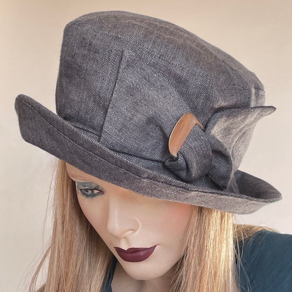 Find this handmade hat by local artisan Sue Scott at Eclection Ottawa. The "Over the Topper" is a smart-looking piece that can easily be dressed up or down. This hat is fashioned in 100% mid-weight herringbone linen fabric in a charcoal shade. The shape has volume with a crown that flares at the top and a wide brim that curves upwards and can be positioned. it is finished off by a large hand-sewn twisted bow and vintage buckle detail and is fully lined. Size large: approximately 22 3/4’’