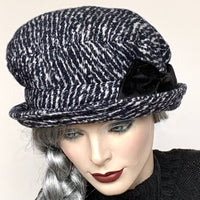 Find this handmade “Judy” hat by local artisan Sue Scott at Eclection Ottawa. It is fashioned in a black and white knit blend of wool, acrylic and cotton which is perfect for the colder months. It features a full two-part crown with some nice volume, a handmade tailored bow trim in black velvet fabric and a small flexible brim. Wind-resistant lining. Size-medium: 22 ½.’’  Please note that the colour can read as a very dark blue in some lightning.