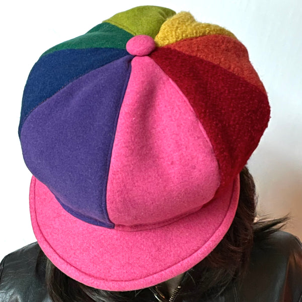 This Casquette is fashioned in a mix of different fabrics that goes from wool flannel,  cashmere and wool blend to 100% wool coating. The shape is an eight-part crown, with some volume and a front peak where each part of the crown is made with a different colour. Red, candy pink, purple, indigo blue, forest green, chartreuse, yellow and Orange. Candy Pink peak and covered button on top. Wind-resistant lining. Size M/L: 22 1/2’’ with an elastic in the back.
