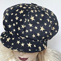 Find this one-of-a-kind Casquette, handmade by local artisan Sue Scott at Eclection Ottawa. It is fashioned in a very fine and soft cotton blend corduroy fabric featuring an allover star print in cream on an ink blue background. The shape is an eight-part crown, with some volume and a front peak. It is finished off with a vintage button on top and sports a fun rainbow print lining inside. Size medium-large: Approximately 22 1/2’’ with an elastic in the back. 