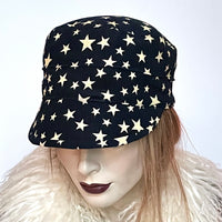 Find this one-of-a-kind Crumper hat, handmade by local artisan Sue Scott, at Eclection Ottawa. It is fashioned in a very fine and soft cotton blend corduroy fabric featuring an allover star print in cream on an ink blue background. The shape is a straight-sided, flat-topped crown, with a classic front peak that conveniently keeps snow off of your eyelashes. It is fully lined with a satiny, flannel-backed Kasha lining that’s easy on the hair and stops the wind. Size-med: Approximately 22 1/2" 