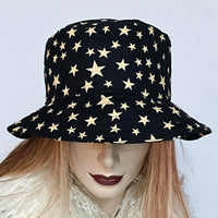 Find this handmade "Nina" bucket hat by local artisan Sue Scott at Eclection Ottawa. It is fashioned in a very fine and soft cotton blend corduroy fabric featuring an allover star print in cream on an ink blue background.  The shape is a classic bucket with a straight-sided crown with a flat top and a topstitched medium brim that angles down. The "Nina" is fully lined with a satiny, flannel-backed Kasha lining that’s easy on the hair and stops the wind. Size-medium: Approximately 22 1/2"
