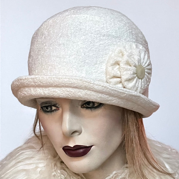 This Cloche hat is fashioned in a classic winter white wool blend with a beautiful, soft and cozy texture. It is finished off with a matching hand-sewn rosette trim adorned with a vintage hand-cut mother-of-pearl button at its center. It is lined with a windproof lining that’s easy on the hair and stops wind for added warmth and features a small, style-able brim with a top stitch. Size-medium: Approximately 22 ½.’’