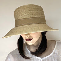 Find this asymmetrical hat at Eclection Ottawa. The “Harper” has an oval, slightly rounded crown with straight sides. Its downward angled wired brim is larger in front  for sun-protection of UPF 50+. It is crafted out of sewn sand colour paper/polyester braid, and  trimmed with a tan polyester grosgrain ribbon finished with white top stitches, and a flat tailored bow in the back. Size medium  22 1/4". With adjustable elastic. UPF 50+. Brim 3 1/4 in front/ 1 3/4" in back. Crown 4 3/4". 