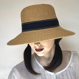 Find this asymmetrical hat at Eclection Ottawa. The “Harper” has an oval, slightly rounded crown with straight sides. Its downward angled wired brim is larger in front  for sun-protection of UPF 50+. It is crafted out of sewn toast/tan colour paper/polyester braid, and  trimmed with a black polyester grosgrain ribbon finished with white top stitches, and a flat tailored bow in the back. Size medium  22 3/4". With adjustable elastic. UPF 50+. Brim 3 1/4 in front/ 1 3/4" in back. Crown 4 3/4". 
