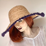 Find this flattering statement hat at Eclection Ottawa. The “Myrtle" is made out of 100% braided raffia pressed into a rounded dome crown. It has a large wireless brim with indigo/purple coloured fringe at the edge and a wide elastic interior band for some adjustability   Size 22 1/2" to smaller. Brim from 5" to 5 3/4". Crown 4 1/2".