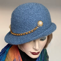 One of a kind, handmade “Regular” hat by a local artisan who is known as "The British Hat Lady". It is hand-knitted in a denim blue 100% wool yarn and then felted into this unique shape. This easy-to-wear shape is finished off with a golden chainette on its side and sports a flexible brim that can be styled easily.  Elegance meets coziness in a very flattering shape for the wintertime. Size: Medium, approximately 22 ½’’.