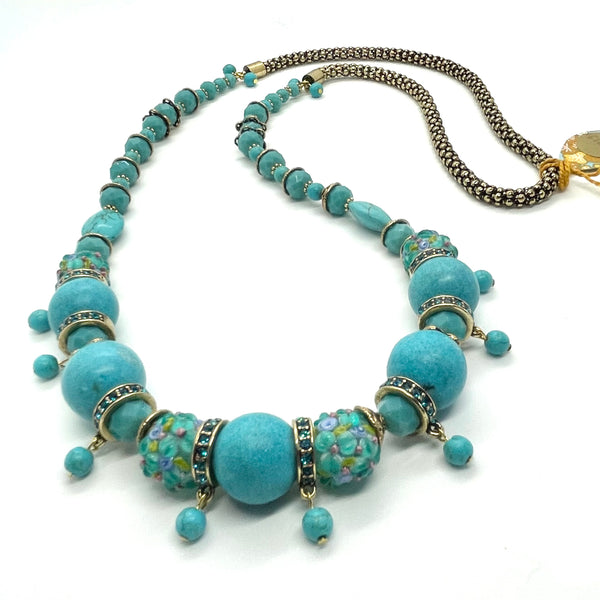 This necklace is carefully crafted with beautifully textured lampwork glass beads, large tinted howlite beads in rich tones of turquoise, crystals, tiny gold-plated flower separator beads, bronze separator beads and findings. It is securely strung by hand on a heavy coated multi-strand tiger tail cord and is lengthened with a crocheted look bronze chain at the nape of the neck. It measures approximately 33 3/4".