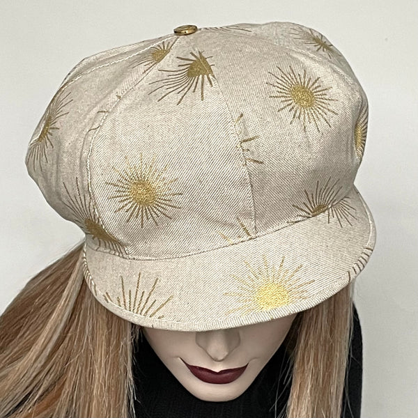 This hat, handmade by local artisan Sue Scott, is called the "Casquette". The fabric is a  mid-weight linen look cotton/polyester blend with a natural background and is enlivened by a decorative gold suns printed motif. The shape is a classic eight-part voluminous crown, with a front peak that protects from the sun. The trim is a matching gold metal button on top which finishes off this hat beautifully. Fully lined with rayon. Size-medium: 22 1/2’’ with elastic in the back that gives it some give.