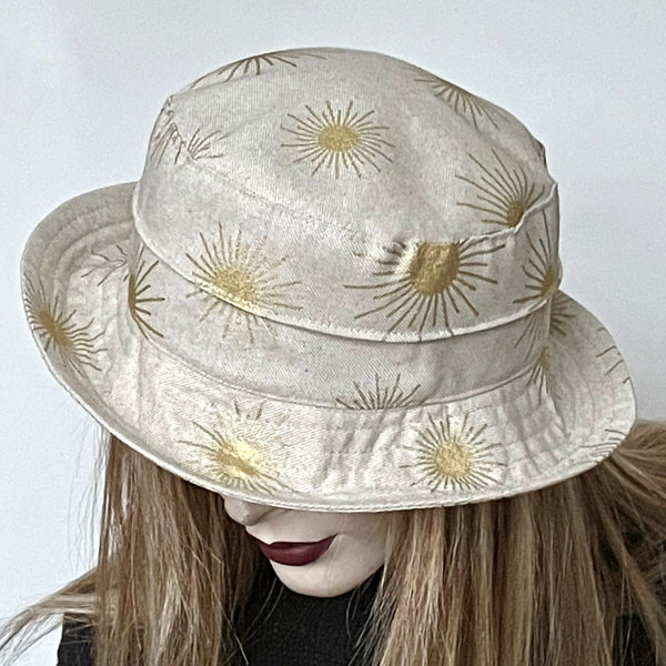 This one-of-a-kind hat, handmade by local artisan Sue Scott, is called the "Jojo". It's a practical and elegant shape that provides sun protection with style. The fabric is a mid-weight linen look cotton/polyester blend with a natural background and is enlivened by decorative gold suns printed motif. The shape is a straight-sided crown with a flat top, with a medium top-stitched brim that curves upwards and can be positioned. Fully lined with satin. Size-medium: 22 1/2’’