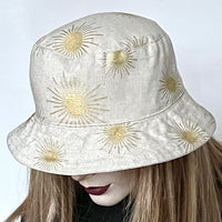 This one-of-a-kind bucket hat, handmade by local artisan Sue Scott, is called the "Nina". The fabric is a medium-weight linen look cotton/polyester blend in beautiful gold sun print on a natural coloured background. The shape is a classic bucket style with a straight-sided crown with a flat top, and a medium brim that angles down for sun protection or can be flipped and curved upwards. Super simple and easy to wear, the "Nina" is fully lined with matching dupioni silk. Size-medium: 22 1/2’’  