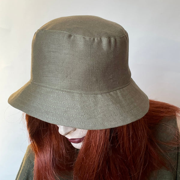 This one-of-a-kind bucket hat, handmade by local artisan Sue Scott, is called the "Nina". The fabric is 100% lightweight linen in a beautiful and versatile sage green shade. The shape is a classic bucket style with a straight-sided crown with a flat top, and a medium brim that angles down for sun protection when styled flat or can be flipped and curved upwards. Super simple and easy to wear, the "Nina" is fully lined with satin. Size-medium: 22 1/2’’  