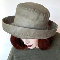 This one-of-a-kind sun hat, handmade by local artisan Sue Scott, is called the "Thomasina". It's a practical and elegant shape that provides great sun protection with style.  The fabric is 100%  lightweight linen in a beautiful and easy-to-wear Sage green shade. The shape is a straight-sided 3 part crown with a flat top and a generous 3 part kettle brim of 2 1/4" wide with a 2" edge that flips up. Fully lined with Bemberg lining. Size-medium: 22 1/2’’